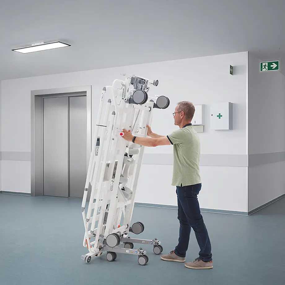 Mitarbeiter transportiert zusammengeklappte Evario one Patientenliege im Klinikbereich.