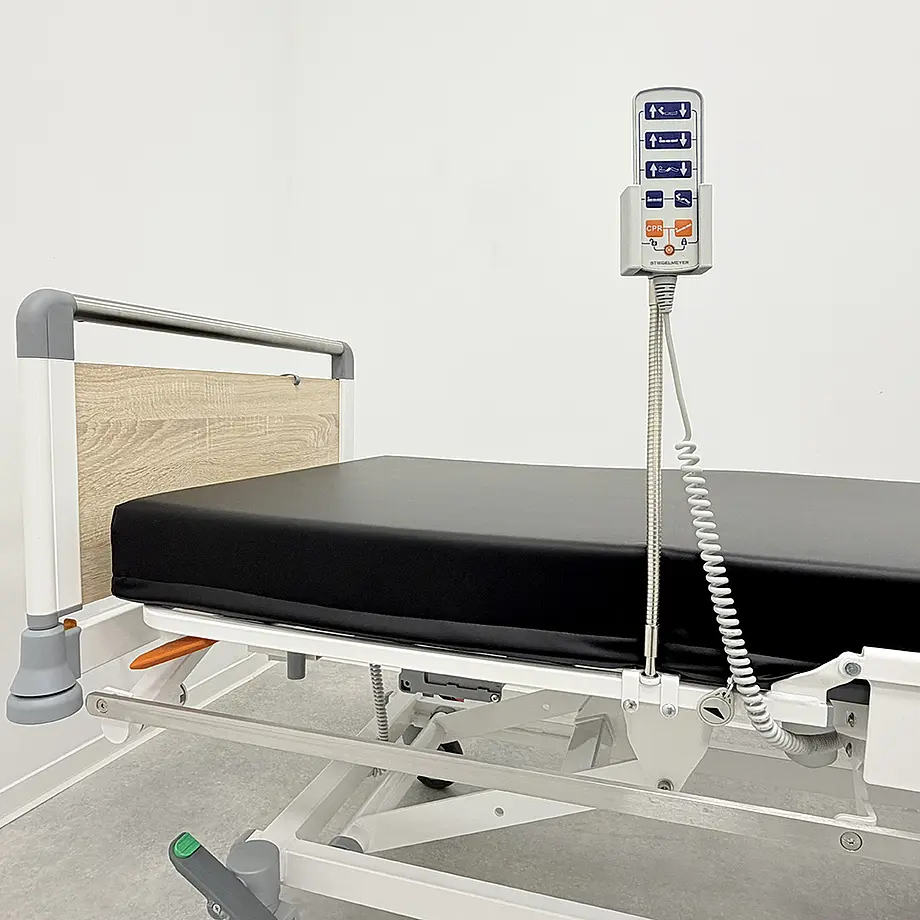 Patientenliege mit befestigter Handschalter-Halterung und Bedienelement am Bettrahmen.